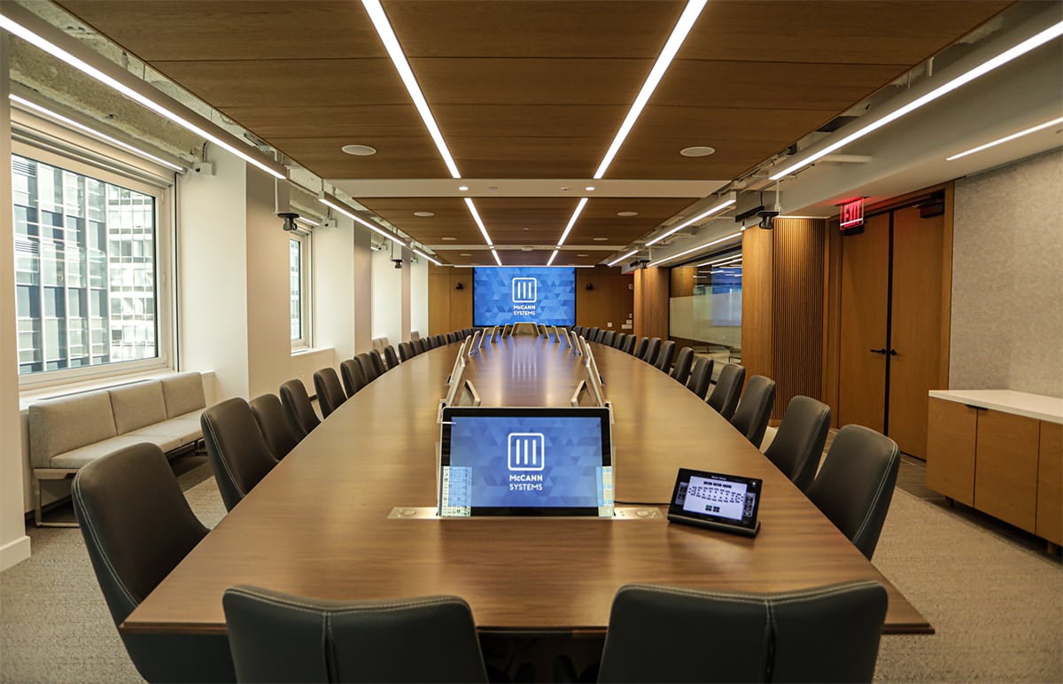 Updated conference room with large video screen at the end of a long table and individual displays for each user.