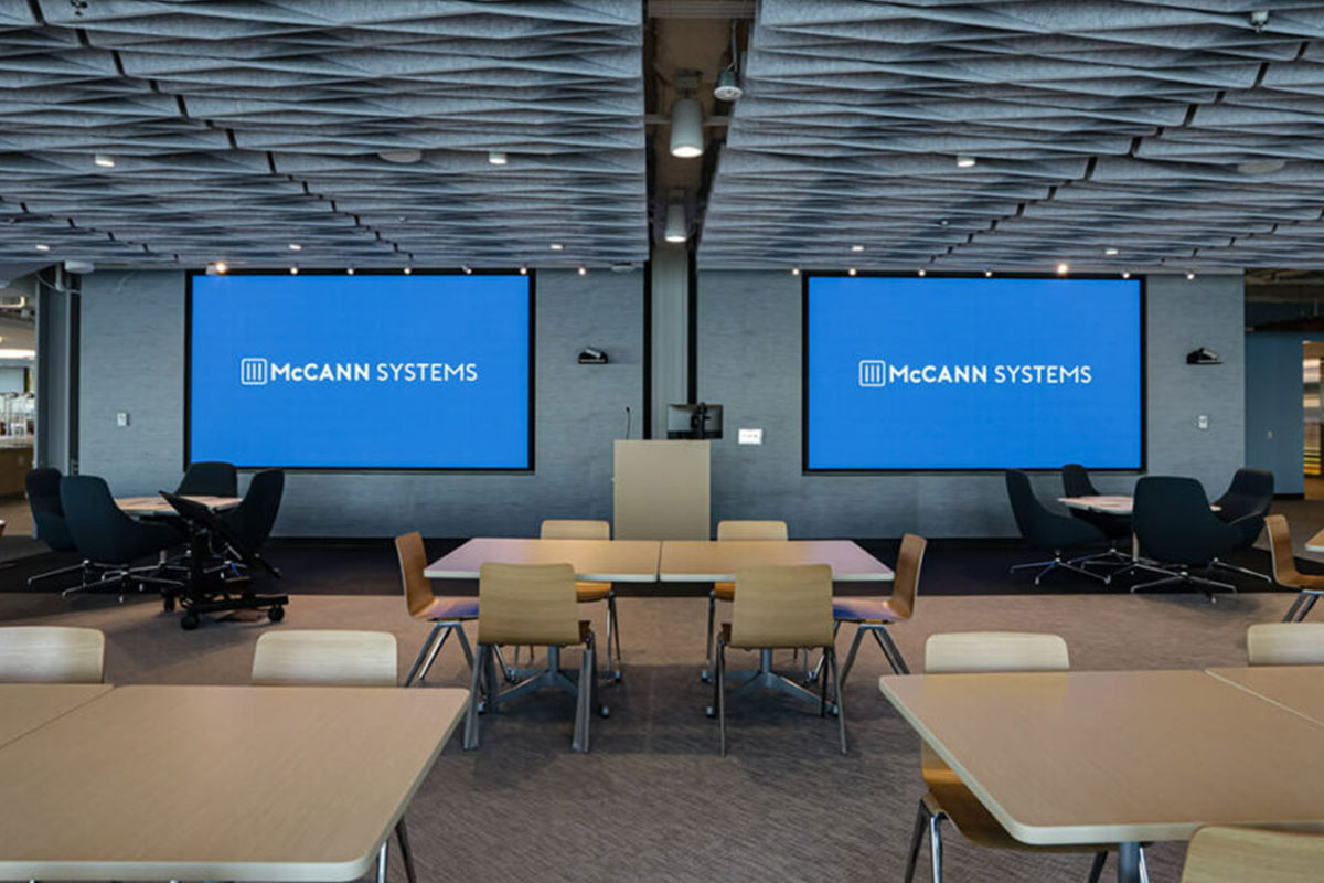 Open plan conference room with two large video screens displaying the McCann Systems logo.