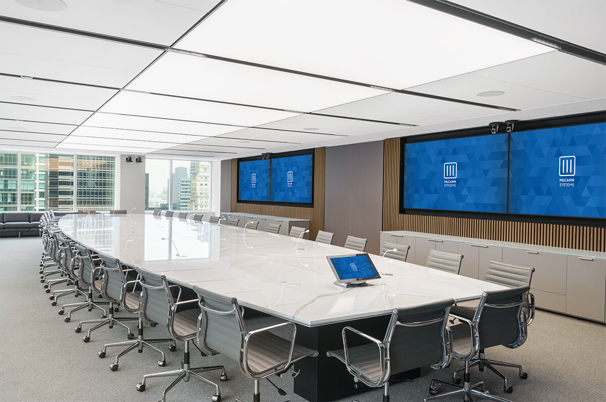 Spacious corporate boardroom with four large flatscreen wall displays and a control panel connected to the table.