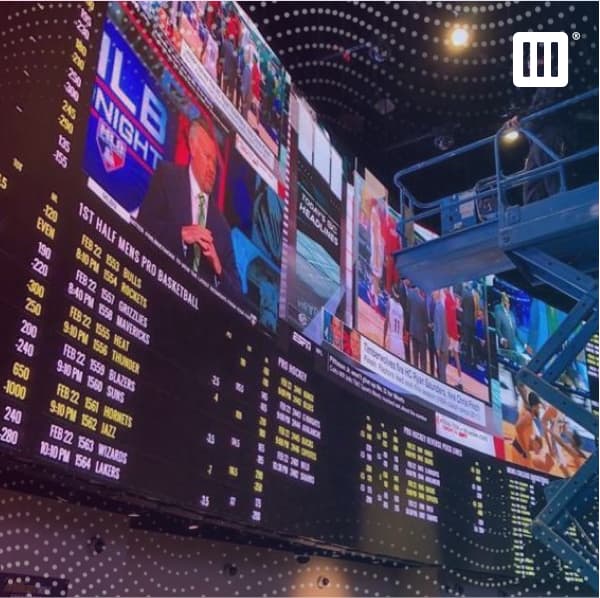 Worker on a power lift inspecting a video wall inside a sportsbook.