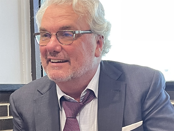 Man in gray business suit with a maroon tie wearing glasses.