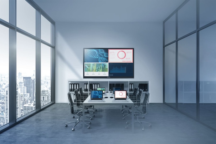 A small meeting room with laptops on the table and a display screen at the head of the room.