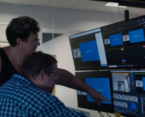 A man and woman in an office pointing at computers.