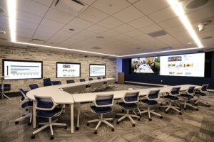 A business video conference room in St. Louis with multiple large displays and a U-shaped table designed for in-person and remote collaboration.