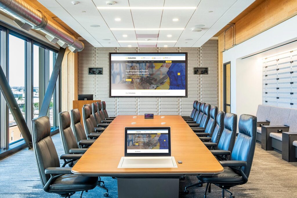 Bright conference room featuring boardroom table, leather chairs, and wall-mounted display screen