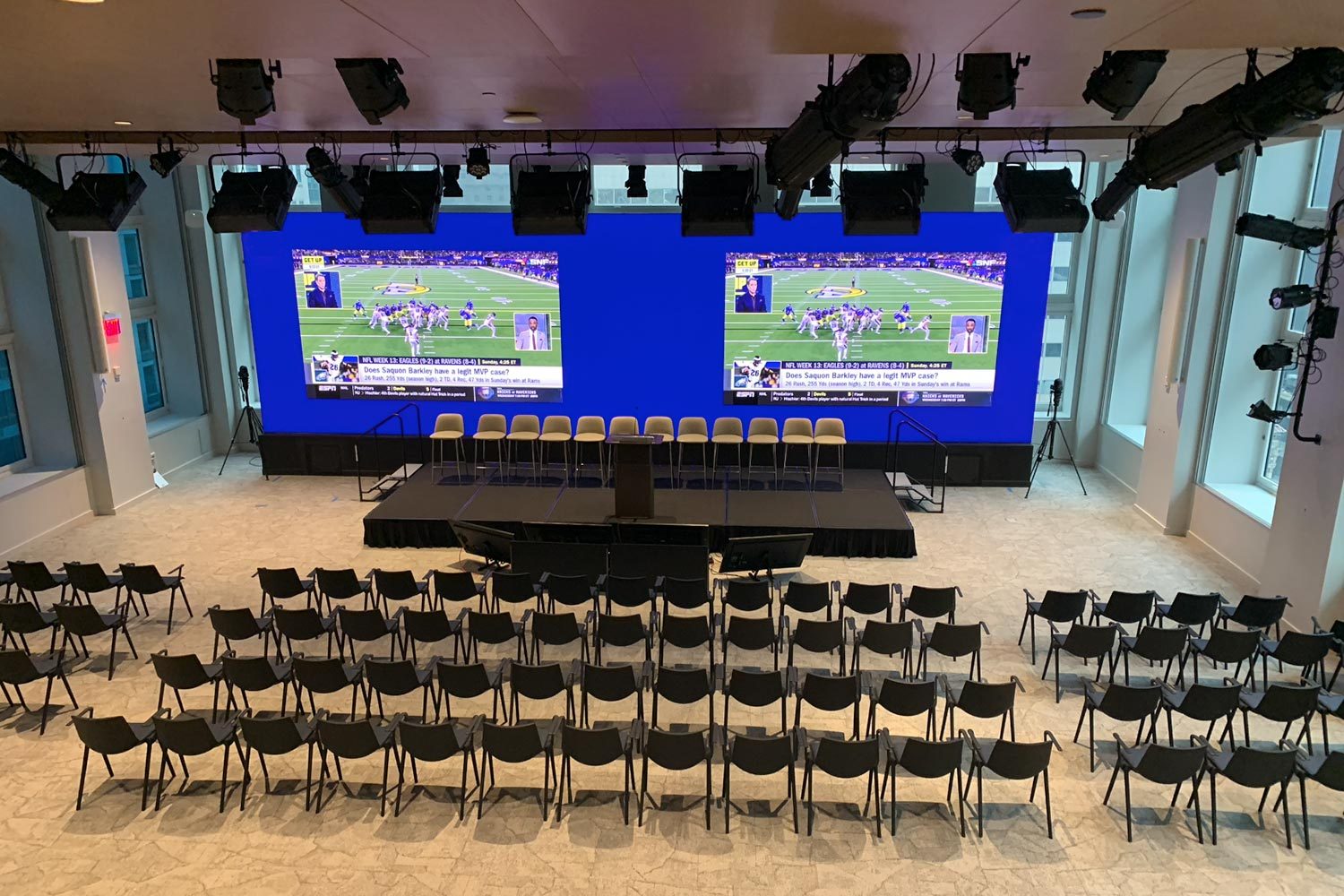 Multi-screen LED display in a conference setting with rows of chairs facing the stage.