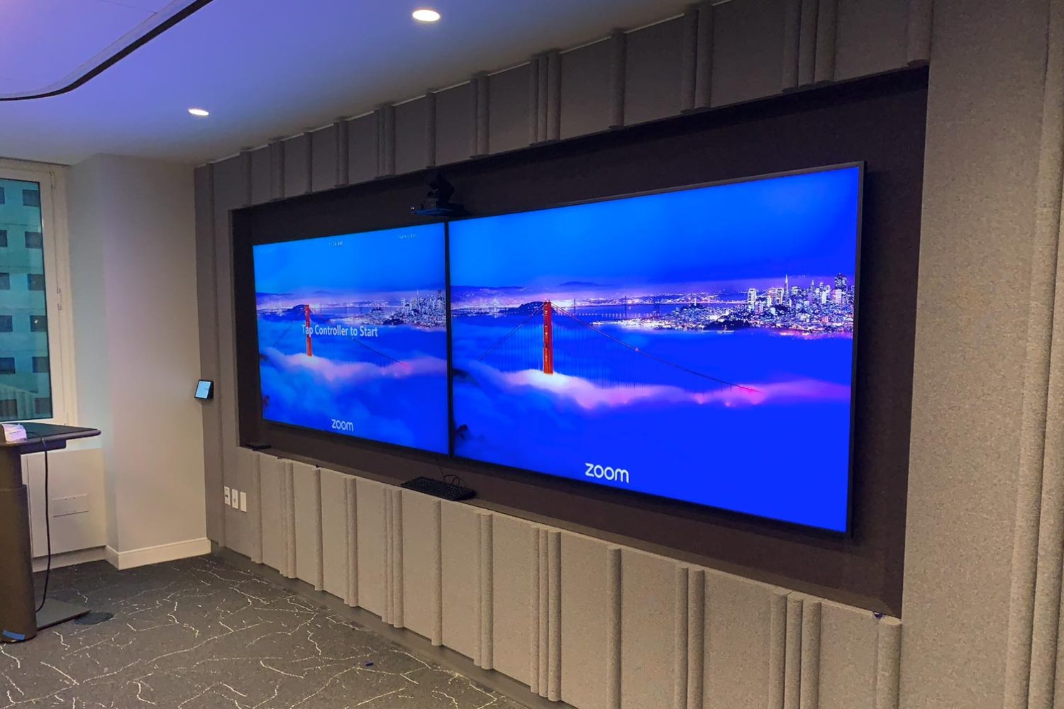 Close-up of dual display screens mounted on a wall in a conference room.