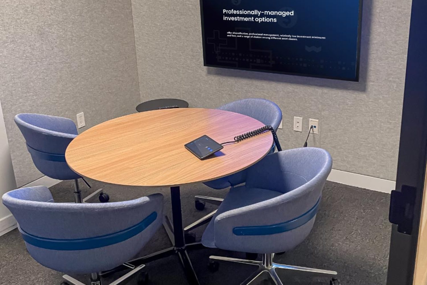 Small meeting room with a round table and a wall-mounted screen for video conferencing.