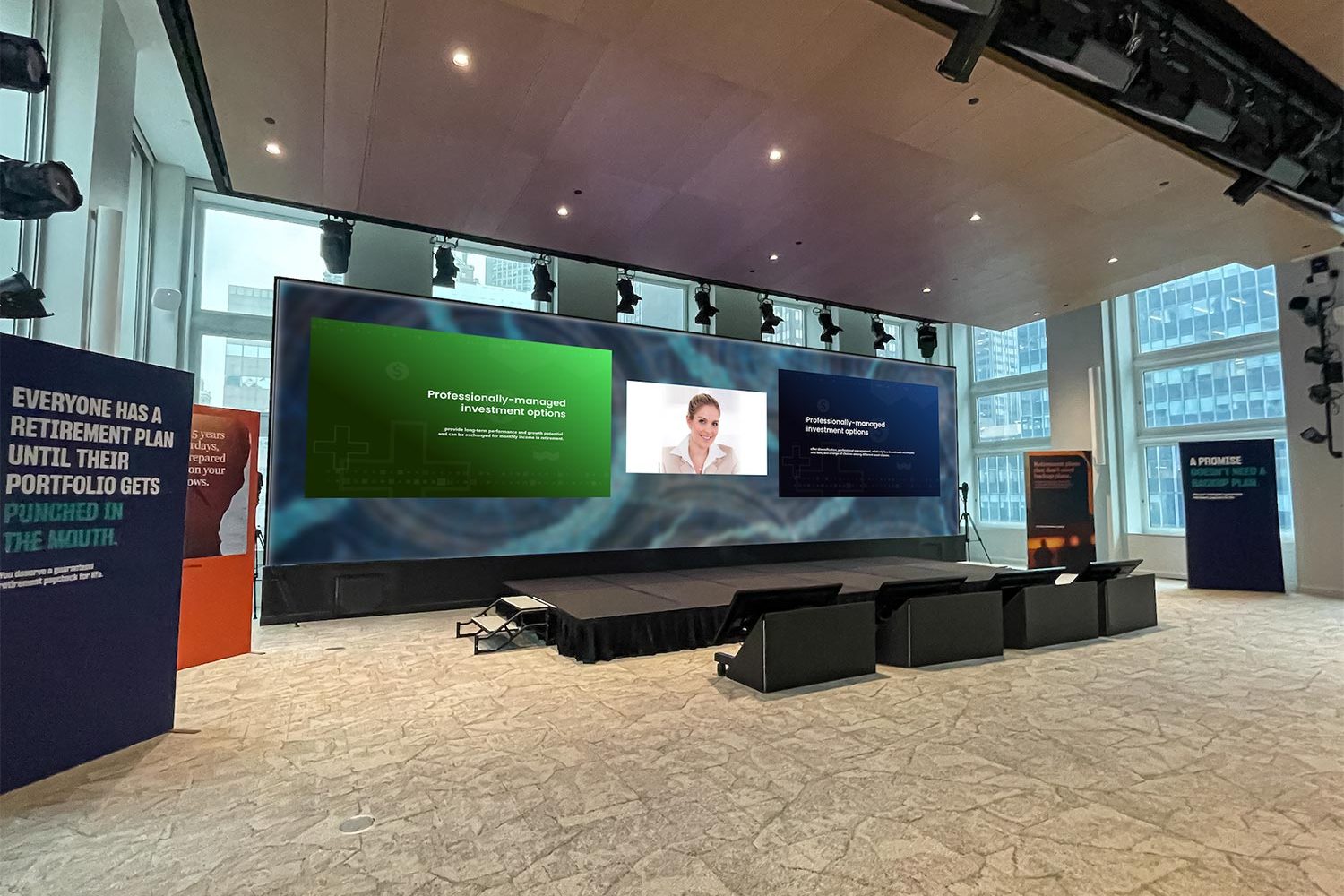 Large LED display in an auditorium showing a split-screen presentation with a speaker’s image.