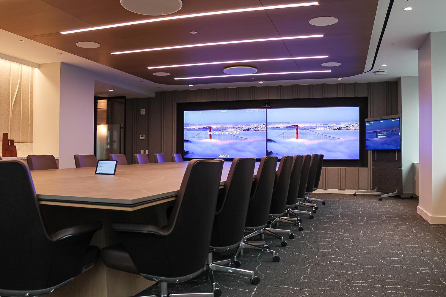 A high-end conference room with a long meeting table, dual screens, and modern lighting.