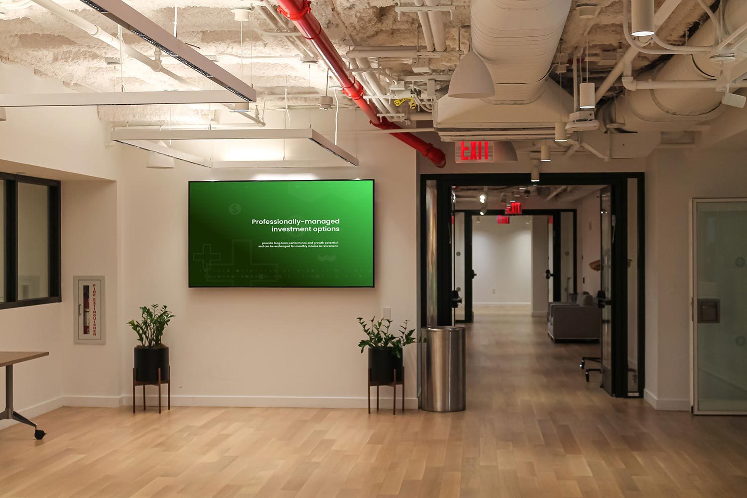 A digital display mounted on a wall in a well-lit office hallway with exposed ceilings.