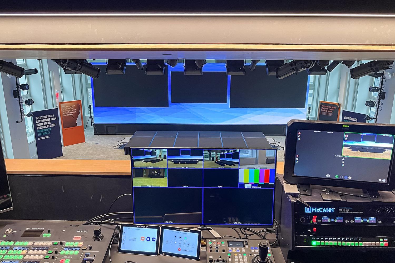 A control room overlooking a stage with multiple monitors displaying live camera feeds and video controls.