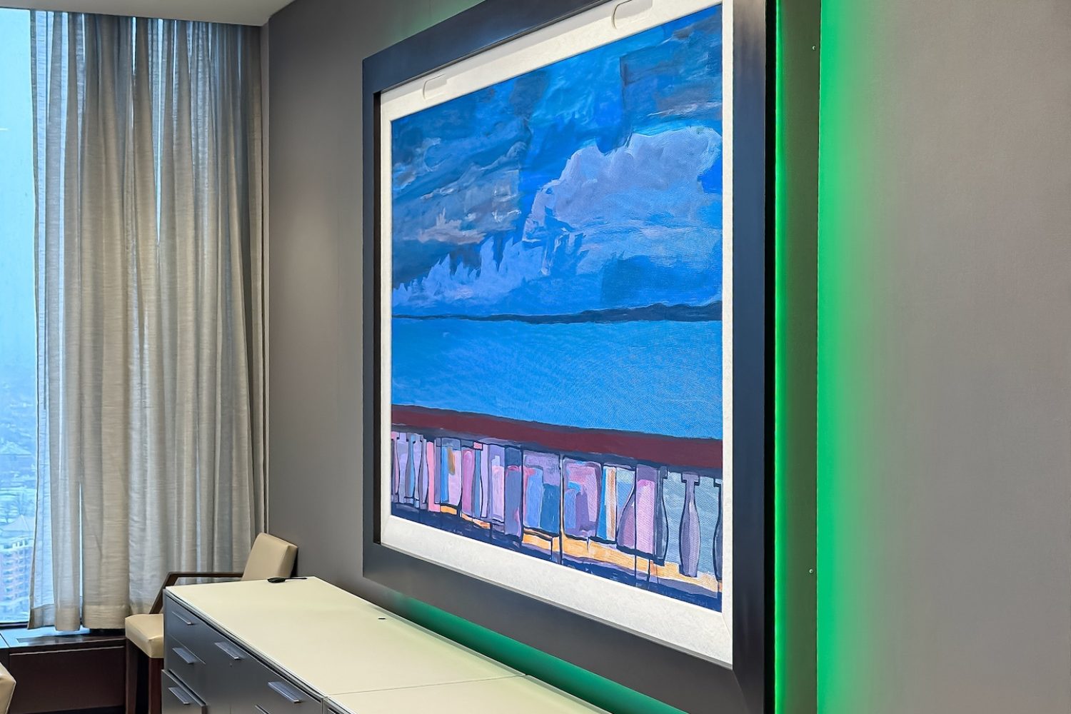 A framed digital artwork in the executive dining space (EDS) with soft green ambient lighting behind it. The cabinetry beneath provides storage, and floor-to-ceiling curtains enhance the luxurious aesthetic.