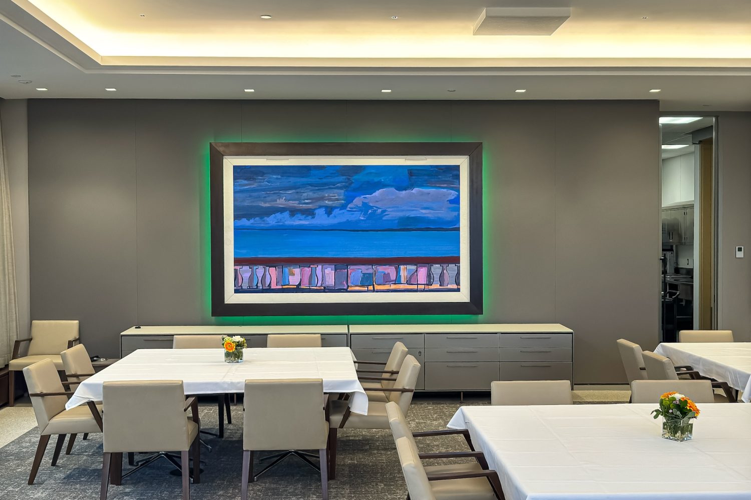 A wider view of the executive dining space, featuring elegant tables with white tablecloths and beige chairs. The digital artwork remains the focal point, with integrated ambient lighting adding a sophisticated touch to the setting.