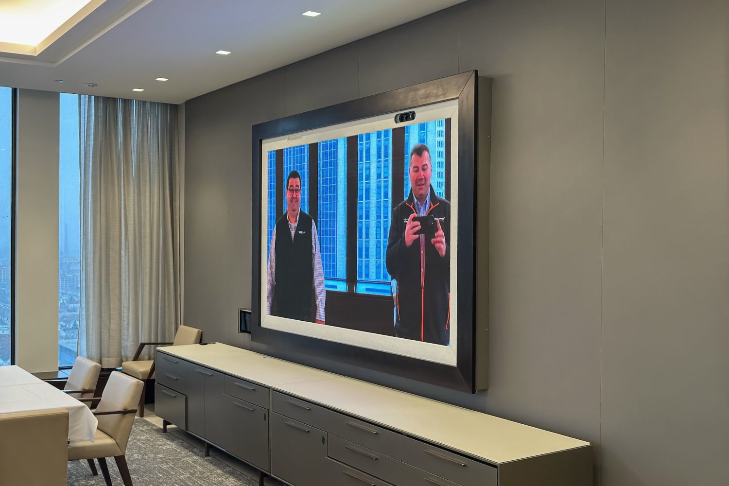 The executive dining space's digital display in use, now showing a live video feed of two presenters, emphasizing the advanced AV capabilities integrated into the space.