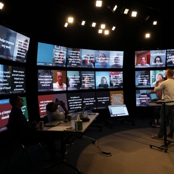 A Proscenium virtual classroom studio is set up with a wall of participant screens with an in-person instructor standing in front of them.