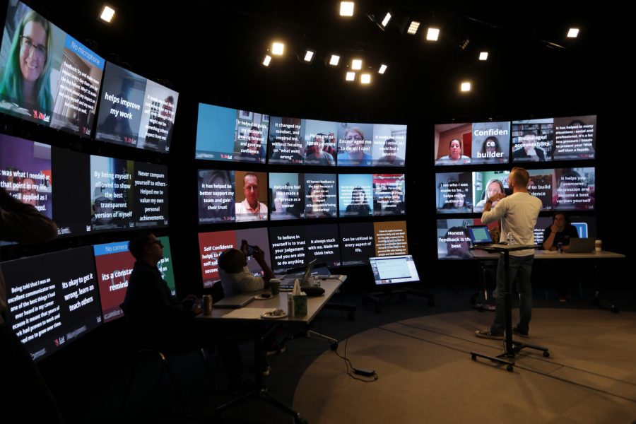 A Proscenium virtual classroom studio is set up with a wall of participant screens with an in-person instructor standing in front of them.