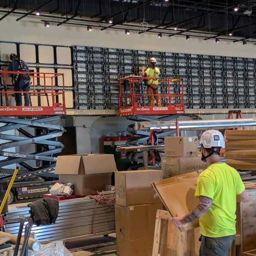 Technicians on lifts installing large LED video wall panels during buildout