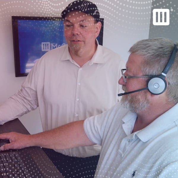 Engineer wearing a head set working on computer while collaborating with a team member.