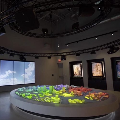 A room with a circular table displaying a colorful scale model of a city.