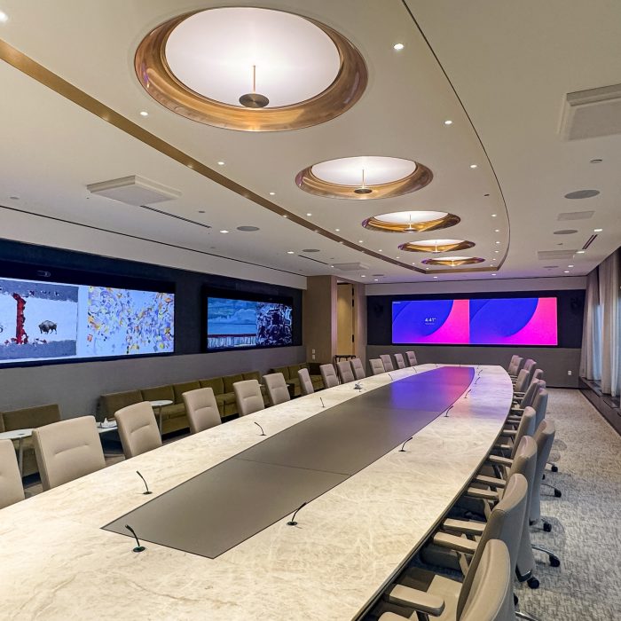 Executive Briefing Center designed for high-profile meetings, strategic planning, and leadership discussions. The space features a state-of-the-art boardroom with an elegant marble conference table, integrated microphones, and advanced AV capabilities. Wall-mounted displays showcase dynamic content, including artwork and corporate presentations, creating an immersive environment for executive decision-making. The sophisticated ceiling design, ambient lighting, and floor-to-ceiling curtains enhance the luxurious and modern atmosphere of the space, reflecting McCann Systems' expertise in AV integration and future-proof communication solutions.