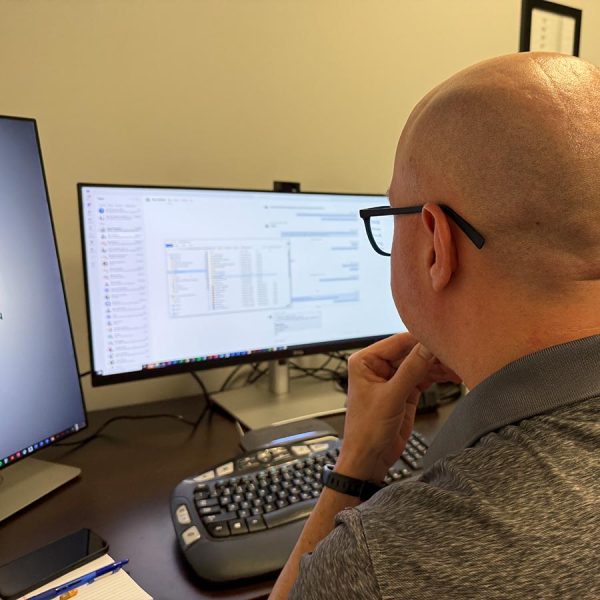 Man reviewing schedules on a large monitor setup at his desk in an office