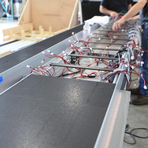 A close-up of electronic components and wiring being assembled on a long table.