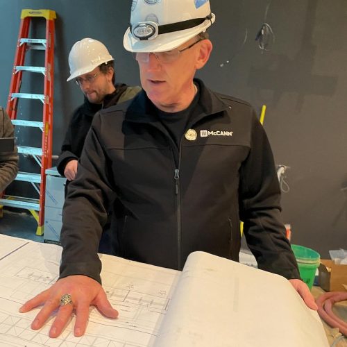 A man in a hard hat examining blueprints on a construction site.