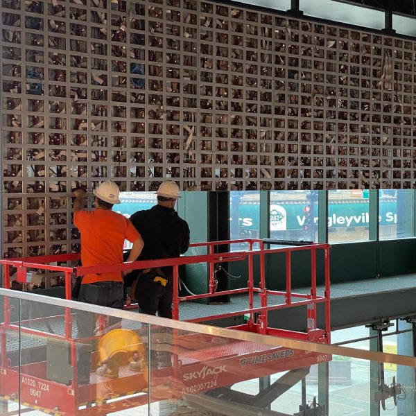 Two men in hard hats working on an installation from a lift inside a large space.