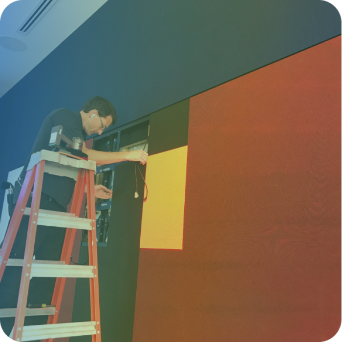 Technician standing on a ladder to work on AV wiring in the wall.